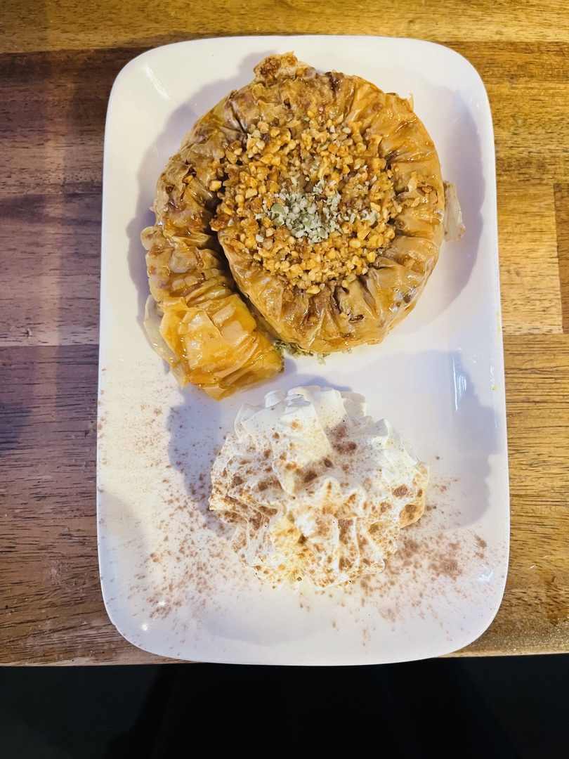 Baklava — a golden coil topped with crushed pistachio, beside a swirl of cinnamon-dusted cream