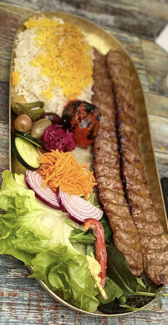 Koobideh — two charcoal-grilled minced kebabs on saffron rice with grilled tomato, pickles and salad on a gold tray, ready to take away