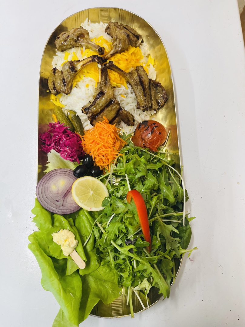 Shishlik — grilled lamb cutlets over saffron rice with joojeh chicken, charred tomatoes and salad on a gold tray