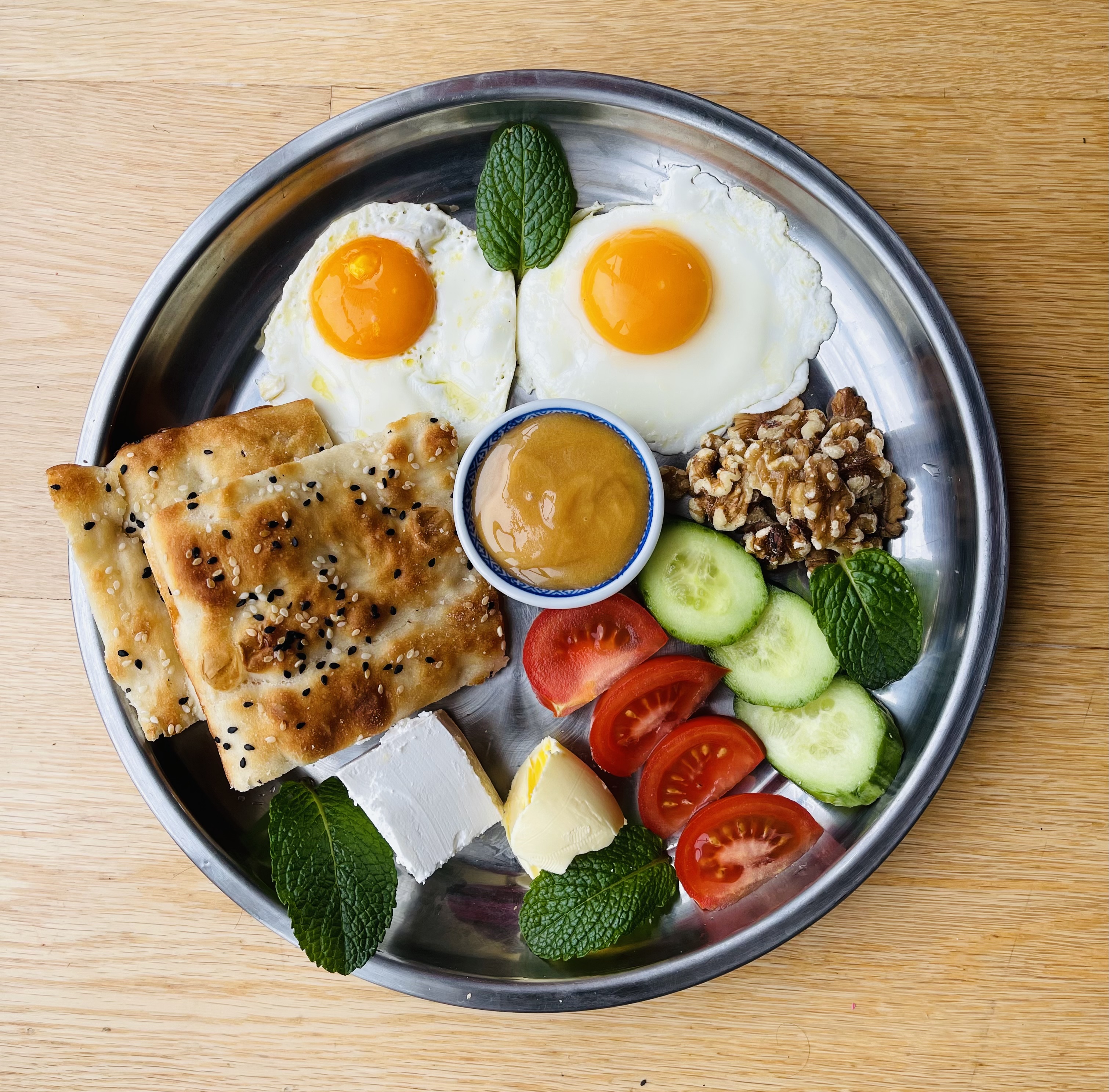 A Persian breakfast plate at Akdeniz — fried eggs, sesame barbari flatbread, feta, walnuts, tomato and cucumber on a silver tray